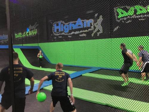 A group of people playing dodgeball on a trampoline court surrounded by green and black walls.