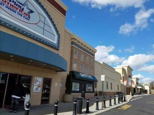 Exterior view of a shopping center with a fun center entrance and various storefronts under a blue sky.