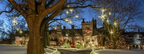 A beautifully lit mansion surrounded by trees and festive decorations, set against a twilight winter sky.