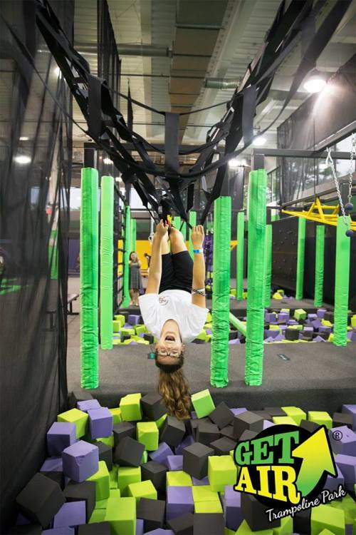 A girl hangs upside down on a trampoline at Get Air Trampoline Park, surrounded by colorful foam blocks.