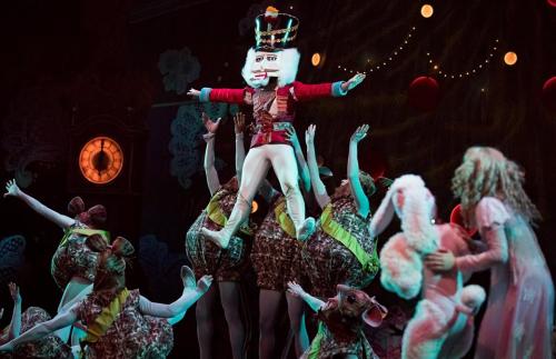 A Nutcracker figure is lifted by dancers in festive costumes during a theatrical performance.