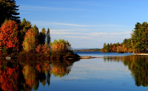 A serene lake surrounded by colorful autumn trees, reflecting the vibrant foliage and clear blue sky.