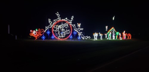 Colorful holiday lights display featuring reindeer, a sleigh, and festive characters against a dark night sky.