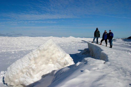 Three people stand on a snowy landscape with large ice formations under a clear blue sky.