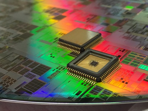 Close-up of two microchips on a colorful, reflective silicon wafer with intricate circuit patterns.