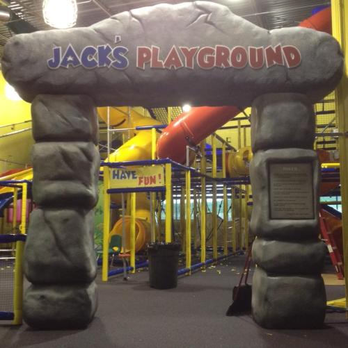 Archway entrance to "Jack's Playground" with colorful play structures and slides in the background.