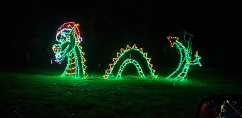 A colorful light display of a dragon wearing a Santa hat, set against a dark background.