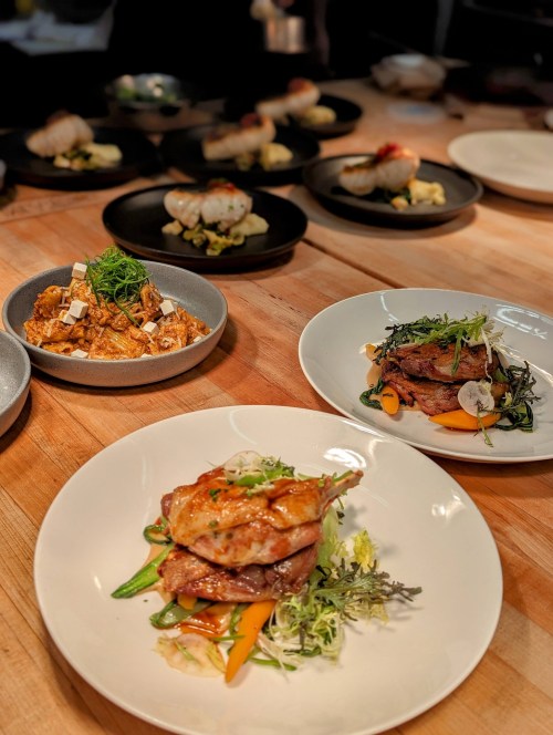 A beautifully plated dish featuring roasted chicken on a bed of vegetables, with other gourmet dishes in the background.