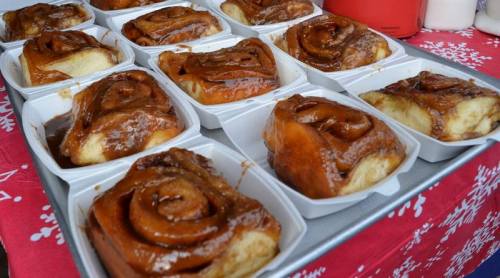 A tray of freshly baked cinnamon rolls, glazed and arranged in white containers on a festive red tablecloth.