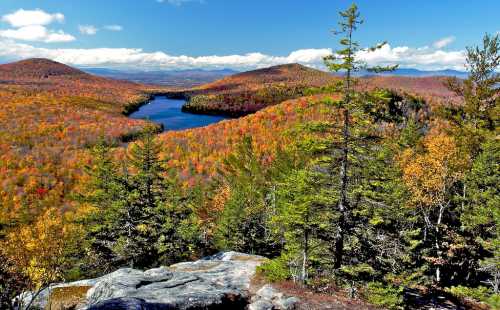 A vibrant autumn landscape featuring colorful trees, a serene lake, and distant mountains under a clear blue sky.