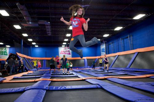 A girl in a red shirt jumps joyfully on a trampoline in a lively indoor trampoline park.