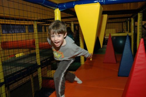 A young boy joyfully plays in a colorful indoor playground, navigating through soft obstacles and climbing structures.