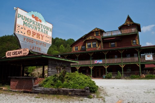 A rustic building with a colorful sign for "Pumpkintown Mountain Opry" and an ice cream shop, surrounded by greenery.