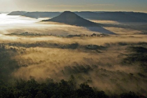 A misty landscape with rolling hills and a prominent peak, bathed in soft morning light.