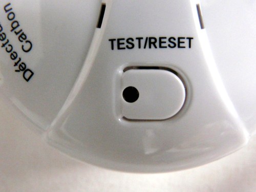 Close-up of a carbon monoxide detector showing the test/reset button and indicator light.