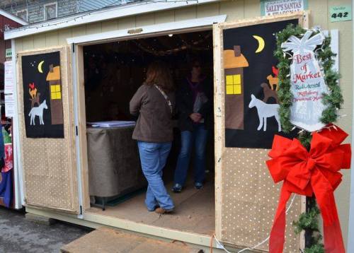A festive market stall with open doors, decorated with holiday lights and a wreath, showcasing a cozy atmosphere.