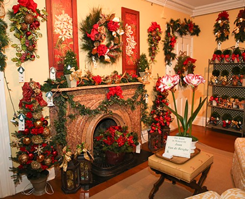 A festive room decorated with holiday wreaths, garlands, and a fireplace adorned with red flowers and greenery.