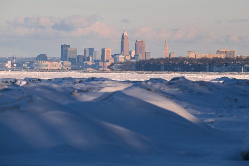 A snowy landscape in the foreground with a view of the Cleveland skyline in the background under a clear sky.