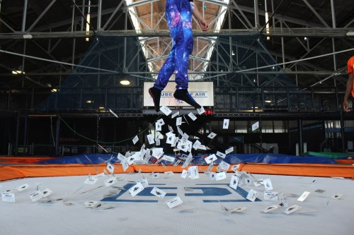 A person in a galaxy-patterned outfit jumps above a trampoline, surrounded by floating cards.