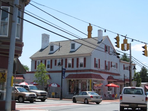 A two-story building with a gray roof and white walls, featuring outdoor seating and traffic lights nearby.