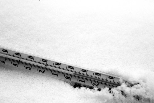 A thermometer partially buried in snow, displaying a temperature reading in a winter landscape.
