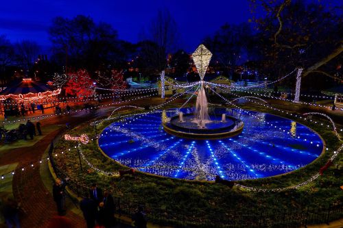 A beautifully lit fountain surrounded by colorful lights and decorations in a park at night.