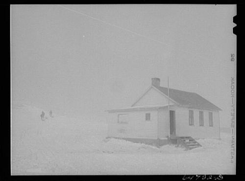 A small white house in a snowy landscape, partially obscured by fog, with two figures walking in the distance.