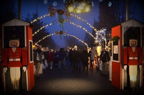 A festive market scene at dusk, with nutcracker decorations and people walking under illuminated arches.