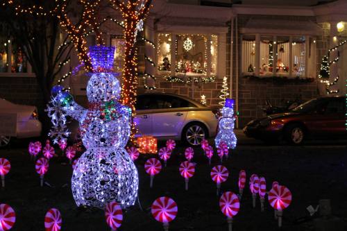 Colorful holiday lights decorate a yard with two illuminated snowmen and candy cane decorations.
