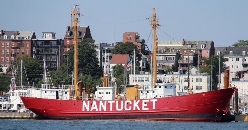 A red ship named "Nantucket" docked near buildings along the waterfront on a clear day.