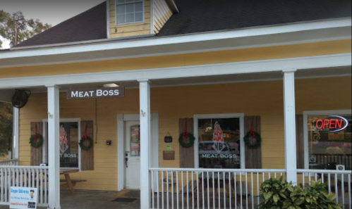 Exterior of a yellow building with a sign reading "Meat Boss" and an "Open" neon sign in the window.