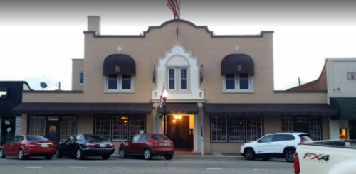 Historic building with a decorative facade, featuring large windows and awnings, set on a street with parked cars.