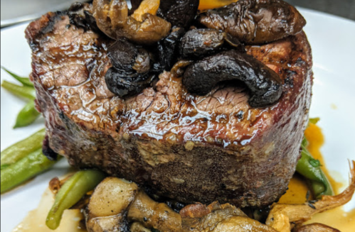 A succulent piece of beef topped with mushrooms, served on a bed of green beans and garnished with sauce.