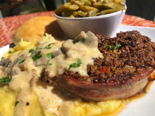A plate of meatloaf topped with gravy, served with mashed potatoes, green beans, and a biscuit.