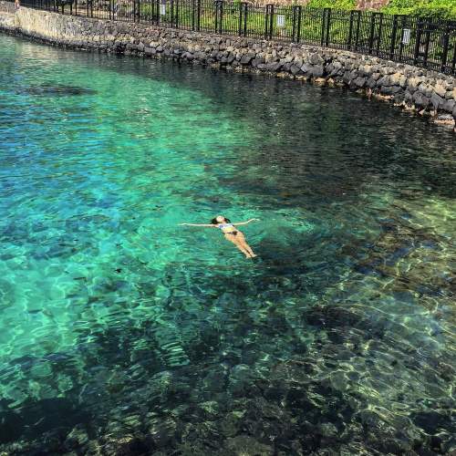 A person floats peacefully in clear, turquoise water near a rocky shoreline.