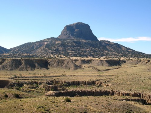 A flat-topped mountain rises above a dry, rocky landscape under a clear blue sky.