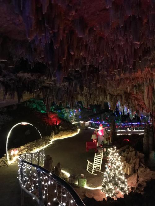 A cave decorated with colorful lights, featuring stalactites, a Christmas tree, and festive decorations along the pathway.