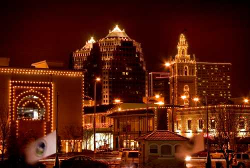 City skyline at night, featuring buildings adorned with festive lights and a decorative tower.