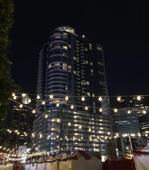 A tall building illuminated at night, surrounded by string lights and tents in an urban setting.