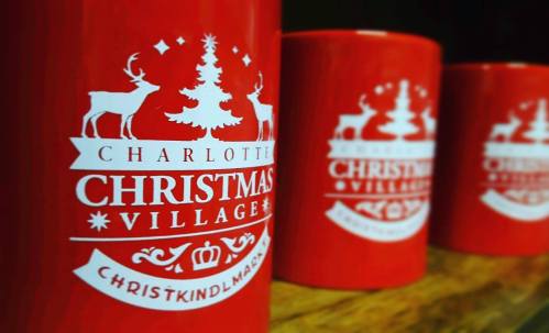 Three red mugs featuring a Christmas Village design with reindeer, a tree, and festive text.