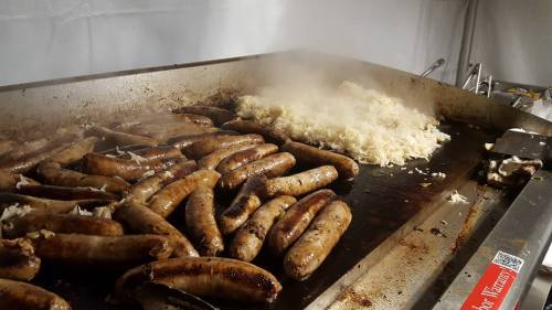 Grilled sausages sizzling on a flat top grill next to a pile of steaming rice.