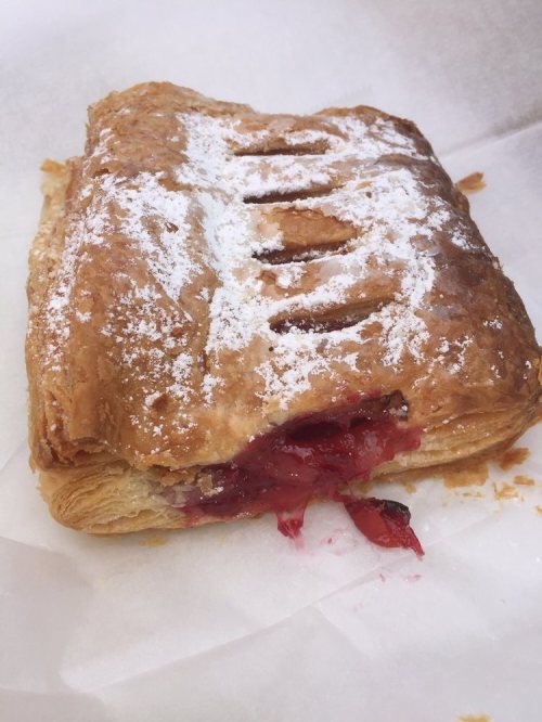 A flaky pastry filled with red fruit filling, dusted with powdered sugar on a white background.
