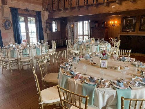 Elegant dining room set for an event, featuring round tables with light blue accents and gold chairs.