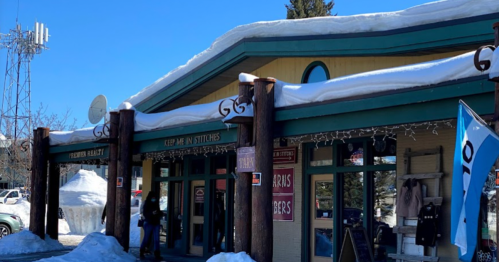 A snowy storefront with wooden pillars, featuring signs for a fabric shop and a nearby cell tower.