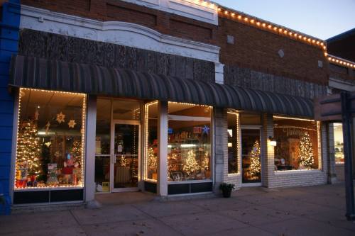 A festive storefront decorated with lights and Christmas trees, showcasing holiday decorations in the windows.