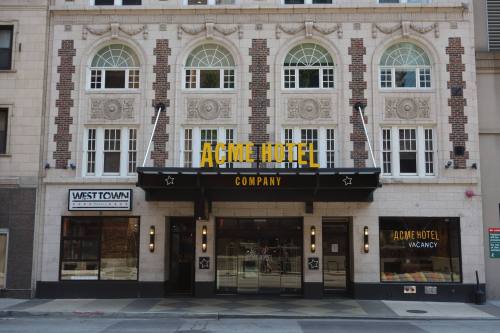 Facade of the Acme Hotel Company featuring large windows and a bright yellow sign, with a "vacancy" notice.