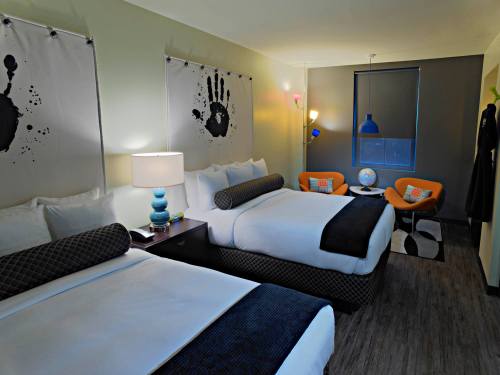 A modern hotel room with two beds, colorful decor, and a seating area featuring orange chairs and a globe.
