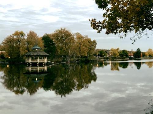 A serene lake scene with a gazebo, surrounded by trees reflecting on the water under a cloudy sky.