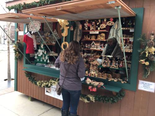 A woman browses handmade crafts at a festive market stall decorated for the holidays.