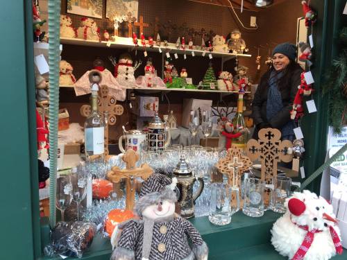 A festive shop window displays holiday decorations, plush toys, and various ornaments, with a smiling woman in a blue scarf.